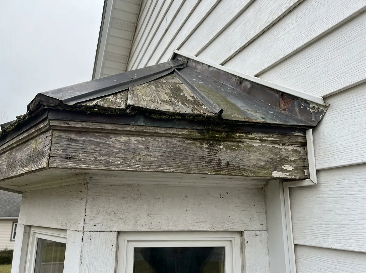 Weathered roof cap of a bay window where metal flashing meets white siding